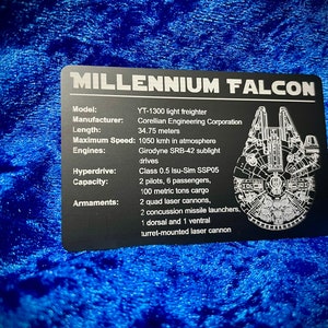May include: A black metal sign with the words "Millennium Falcon" in white lettering. The sign lists the specifications of the Millennium Falcon, including its model, manufacturer, length, maximum speed, engines, hyperdrive, capacity, and armaments.