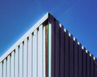 May include: Two white security cameras mounted on a corrugated metal wall. The wall is painted a light blue color and the cameras are facing outward.