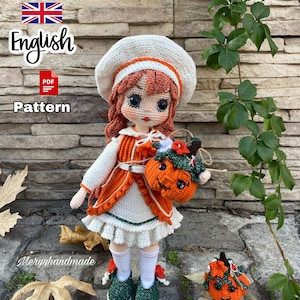 Puede incluir: Muñeca de crochet con un vestido blanco, un suéter naranja y un sombrero blanco. La muñeca sostiene una calabaza naranja de crochet. La muñeca está de pie sobre una superficie de piedra con hojas verdes y una pared de ladrillo en el fondo. El texto "English PDF Pattern" es visible en la imagen.