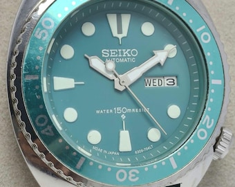 May include: A teal Seiko automatic wristwatch with a silver bezel and teal rubber strap. The watch face is teal with white hands and markers, and the day is displayed as "WED 3". The watch is marked "WATER 150M RESIST".