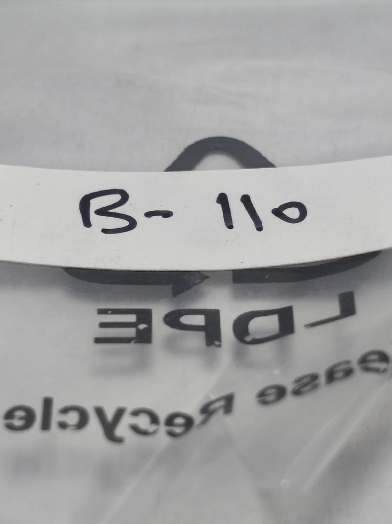 May include: A close-up shot of a white label with the text "B-110" in black. The label is partially obscured by a clear plastic bag with the word "DBE" and other text visible.