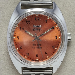 May include: A vintage wristwatch with a silver-tone case and band. The watch face is a copper color with black numerals and hands. The watch face has text in a foreign language. The watch is a classic style.