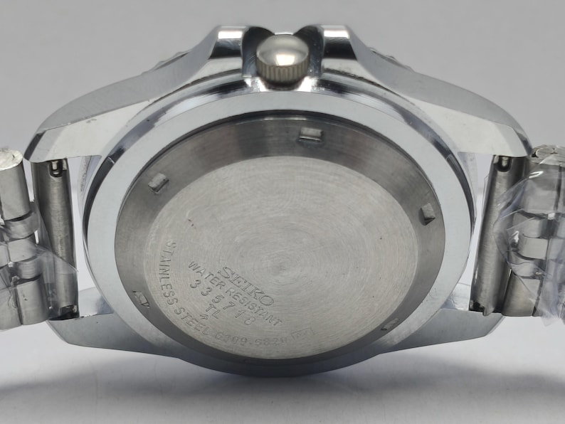 May include: Close-up of a stainless steel Seiko watch. The watch back features the text "SEIKO WATER RESISTANT" and other details. The watch has a silver-colored metal band and a silver-colored case.
