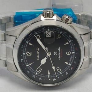 May include: A stainless steel Seiko automatic wristwatch with a black dial, silver-tone hands, and Arabic numerals at the 12, 6, and 10 o'clock positions. The watch features a date window, a rotating inner compass bezel, and a metal link bracelet.