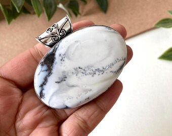 Pode incluir: Um pingente oval branco e preto com uma argola de filigrana prateada. O pingente é feito de uma pedra natural com um padrão de mármore.