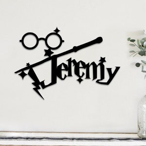 May include: Black metal wall art featuring the name "Jeremy" in a stylized font, with glasses, a wand, and lightning bolt accents. The design is reminiscent of a popular fantasy theme, suitable for home decor.