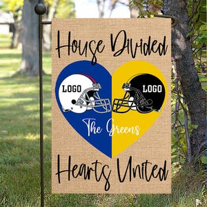 May include: A burlap garden flag with the text "House Divided Hearts United." The flag features a blue and yellow heart design with football helmets and the text "The Greens." The flag is hanging on a black metal pole.