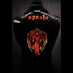 Puede incluir: Chaqueta de cuero negra con la palabra "apashe" en letras rojas en los hombros. La parte trasera de la chaqueta presenta un gran gráfico de una figura vestida con alas en tonos rojos y naranjas.