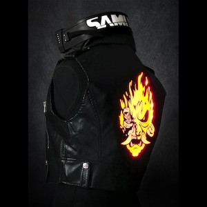 May include: Black leather vest with a reflective yellow and orange graphic of a flaming skull on the back. The vest has a zip closure and a small pocket. A black collar with the word "SAM" in white is visible.