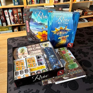 Könnte beinhalten: Brettspielboxen und Komponenten werden gezeigt. Die Boxen zeigen den Spieletitel "Raine" mit Wasser- und Blumenkunst. In der geöffneten Box befinden sich Spielsteine, Karten und ein Spielbrett. Das Spiel scheint ein Strategie- oder Abenteuerspiel zu sein.