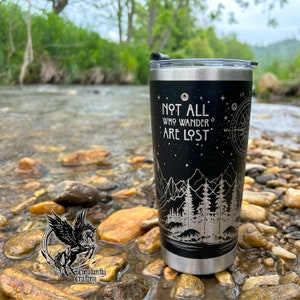 May include: A black stainless steel tumbler with a white design of a mountain range, trees, and stars. The tumbler has the text "Not all who wander are lost" on the front.