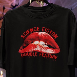 May include: Black t-shirt featuring a graphic of red lips with the words "SCIENCE FICTION DOUBLE FEATURE" in red text. The design has a vintage, horror movie aesthetic.