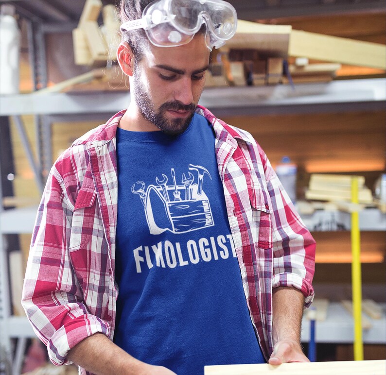 A man wearing safety glasses and a red and white plaid shirt over a royal blue t-shirt with a white graphic of a toolbox and the text "Fixologist".