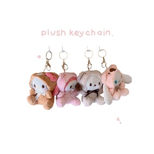 May include: Four plush keychain characters with key rings. The characters are a brown bear, a pink bear, a pink bunny, and a brown cat. The characters are all wearing different outfits.