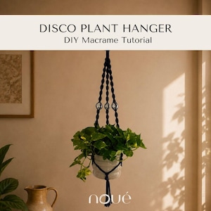 Puede incluir: Un colgador de plantas de macramé azul oscuro con tres cuentas de bola de discoteca reflectantes, que sostiene una maceta de cerámica blanca con una planta pothos verde. El texto DISCO PLANT HANGER DIY Macrame Tutorial aparece arriba.