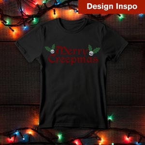 Op de afbeelding: Zwart T-shirt met een rode "Merry Creepmas" afbeelding met schedels en hulstbladeren.