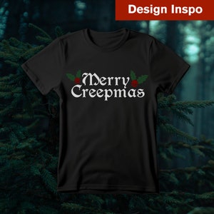 Op de afbeelding: Zwart T-shirt met een witte afbeelding met de tekst "Merry Creepmas" met rode en groene hulstaccenten.
