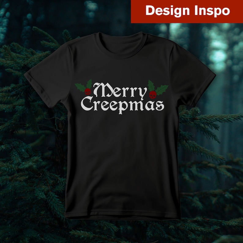 Op de afbeelding: Zwart T-shirt met een witte afbeelding met de tekst "Merry Creepmas" met rode en groene hulstaccenten.