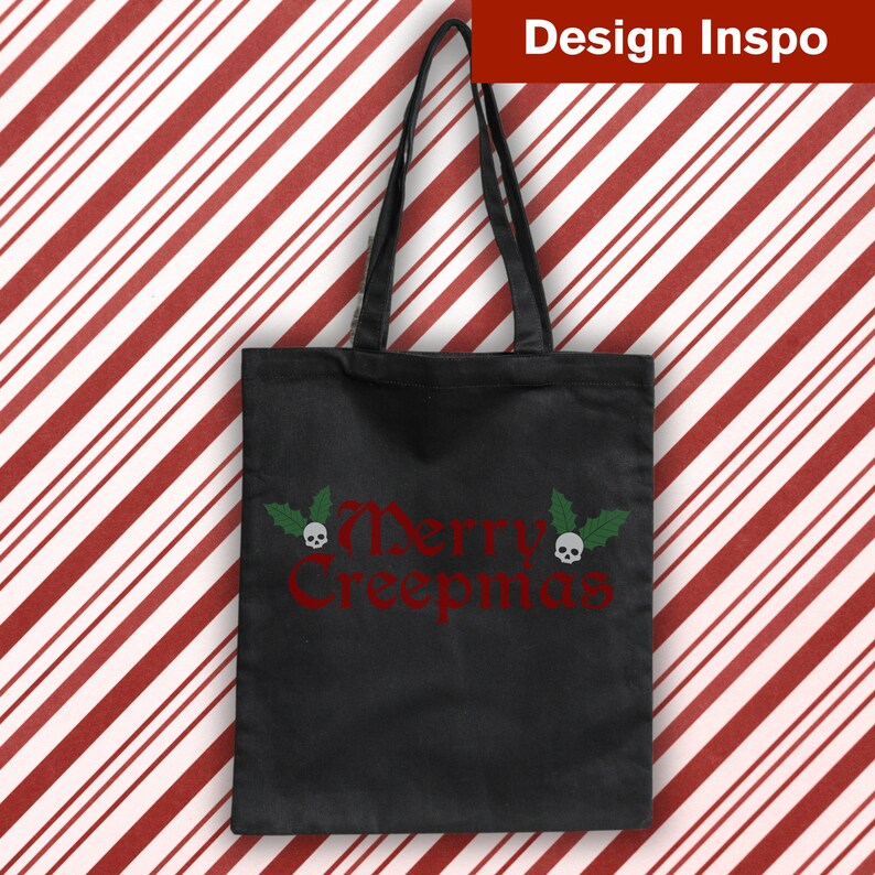 Op de afbeelding: Zwarte tote bag met een rood "Merry Creepmas" ontwerp met twee schedels met groene hulstbladeren.