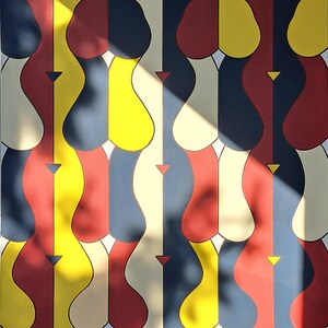 May include: Abstract geometric pattern painting with a repeating design of curved shapes in red, yellow, blue, and cream colors. The painting is lit by a bright light source, casting shadows across the surface.
