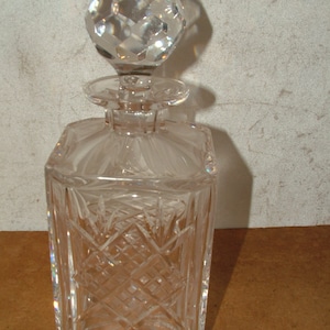 May include: A clear glass decanter with a faceted stopper. The decanter has a square body with a diamond pattern.
