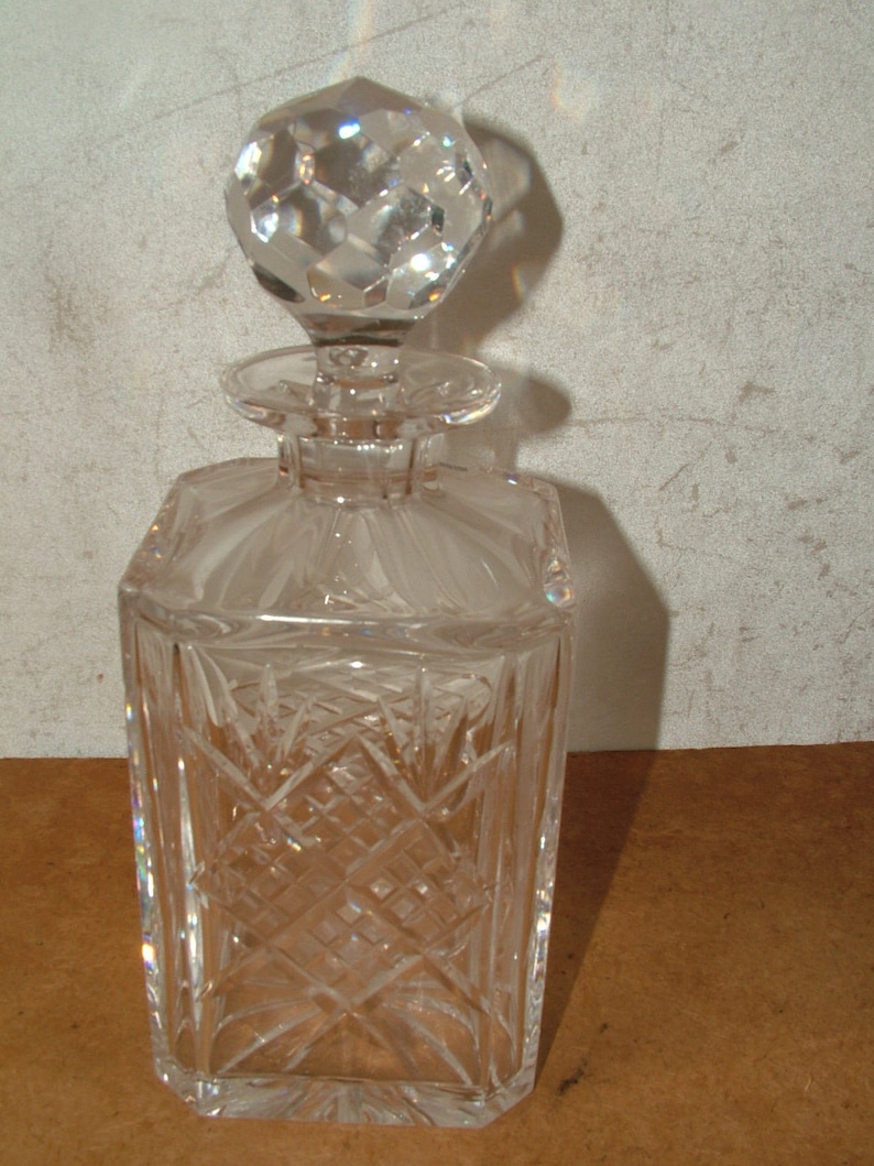 May include: A clear glass decanter with a faceted stopper. The decanter has a square body with a diamond pattern.