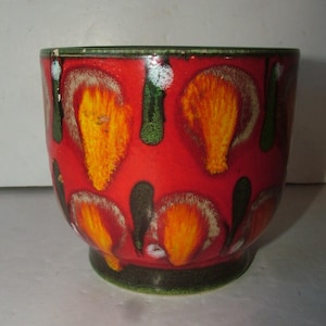 May include: A ceramic planter featuring a vibrant red base colour with repeating orange and yellow flame-like patterns. The design includes dark green vertical accents and a dark green rim and base, creating a bold, multi-coloured appearance.