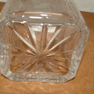 May include: A clear glass decanter with a square base and a starburst pattern on the bottom.