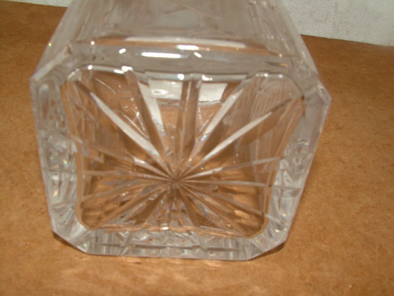May include: A clear glass decanter with a square base and a starburst pattern on the bottom.