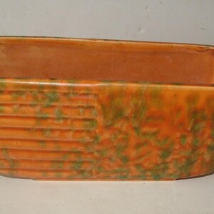 May include: An orange rectangular planter with a curved front and a textured, ribbed design. The planter has green accents and a smooth interior. A decorative item for plants.