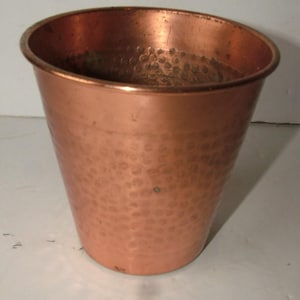 May include: A copper-coloured metal bucket with a hammered texture. The bucket has a slightly tapered shape, wider at the top and narrower at the base. The rim is smooth, and the body features a pattern of small, evenly spaced indentations.