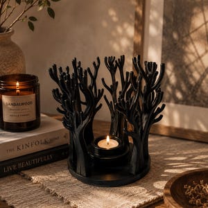 May include: A black candle holder featuring a circular base and a surrounding structure of stylised, leafless tree branches. A small, round tea light candle sits in the centre of the base, with a lit flame casting a warm glow.