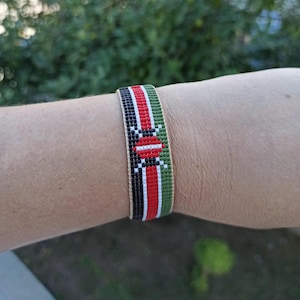 Puede incluir: Una pulsera de cuentas con los colores de la bandera de Kenia. La pulsera es verde, negra, roja y blanca.
