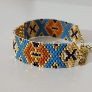 May include: A beaded bracelet with a geometric pattern. The bracelet features a repeating design of blue, orange, and gold beads. The bracelet is adjustable and has a gold-colored chain.