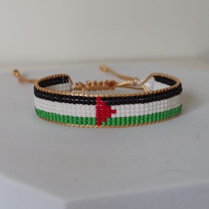 May include: A beaded bracelet with the colors of the Palestinian flag. The bracelet is made with small, colorful beads and has a gold cord closure.