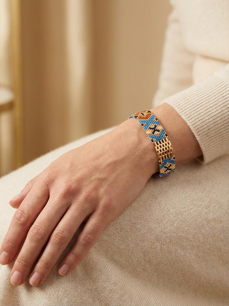 May include: A beaded bracelet with a gold-tone chain and a colorful pattern of blue, orange, and black beads. The bracelet is worn on a wrist, showcasing the intricate design and craftsmanship. The bracelet's design features geometric shapes.