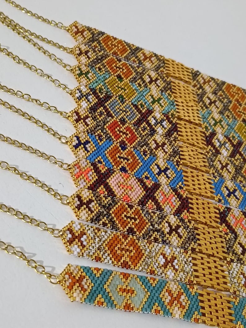 May include: Close-up of several beaded bracelets with gold-colored chain clasps. The bracelets feature intricate geometric patterns in various colors, including orange, blue, white, and brown. The beads are tightly woven together, creating a textured surface.