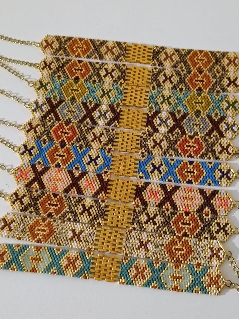 May include: A collection of beaded bracelets with intricate geometric patterns in shades of brown, gold, blue, and orange. Each bracelet features a gold chain clasp. The bracelets are displayed side by side.