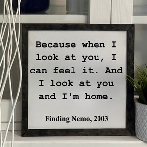May include: Square wooden sign with a white background and black text. The text reads "Because when I look at you, I can feel it. And I look at you and I'm home." Below the text is "Finding Nemo, 2003."