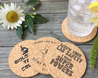 May include: Set of three cork coasters with science-themed designs. The coasters feature a microscope, an atom, and the text "Screw your lab safety I want super powers".