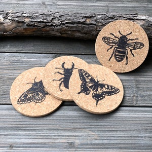 May include: Set of four cork coasters featuring black and white insect illustrations. The coasters feature a bee, a butterfly, a moth, and a stag beetle.