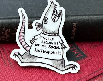 May include: A white sticker with a cartoon illustration of a rat wearing a shirt that says "Sincere Apologies for my Social Awkwardness".