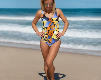May include: A woman wearing a yellow, blue, and orange geometric patterned swimsuit on a beach.