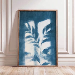 Könnte beinhalten: Ein rechteckiger Wandkunstdruck mit einer botanischen Silhouette großer Blätter in tiefblauen und weißen Tönen, eingefasst in einen schlichten Holzrahmen mit sichtbarer Maserung, der ein kontrastreiches und strukturiertes Bild zeigt.