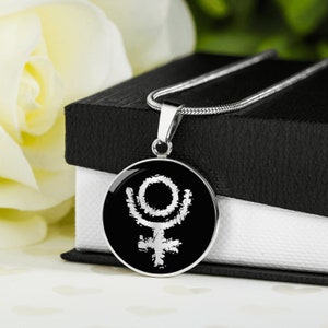 May include: A silver necklace with a black circular pendant featuring a white astrological symbol. The symbol is a circle with a cross inside and a crescent moon shape above the cross.