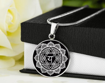 May include: A silver necklace with a black pendant featuring a white mandala design with a Sanskrit symbol in the center. The pendant is round and has a detailed design.