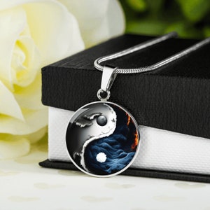 Könnte beinhalten: Eine silberne Halskette mit einem runden Anhänger, der ein Yin-Yang-Symbol mit schwarzen und weißen wirbelnden Mustern und einem weißen Mond auf jeder Seite zeigt.