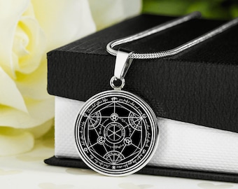 May include: A silver chain necklace with a black circular pendant featuring a detailed white alchemical symbol and inscription. The pendant is on a black velvet box.