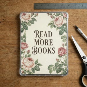 K&ouml;nnte beinhalten: Eine rechteckige, transparente H&uuml;lle mit floralem Design und dem Text "READ MORE BOOKS". Das Design zeigt rosa Rosen und gr&uuml;ne Bl&auml;tter. Ein Metalllineal, eine Schere und ein Bastelmesser sind sichtbar.