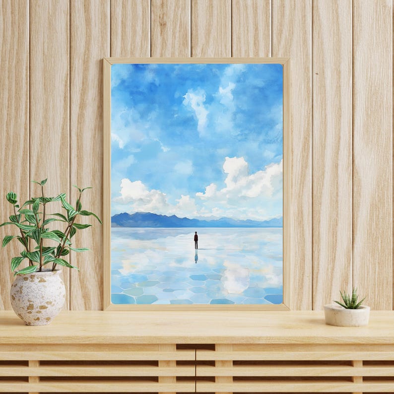 May include: A framed watercolor painting of a person standing in a vast, blue, reflective body of water. The sky is a light blue with white clouds. The mountains in the distance are a hazy blue.